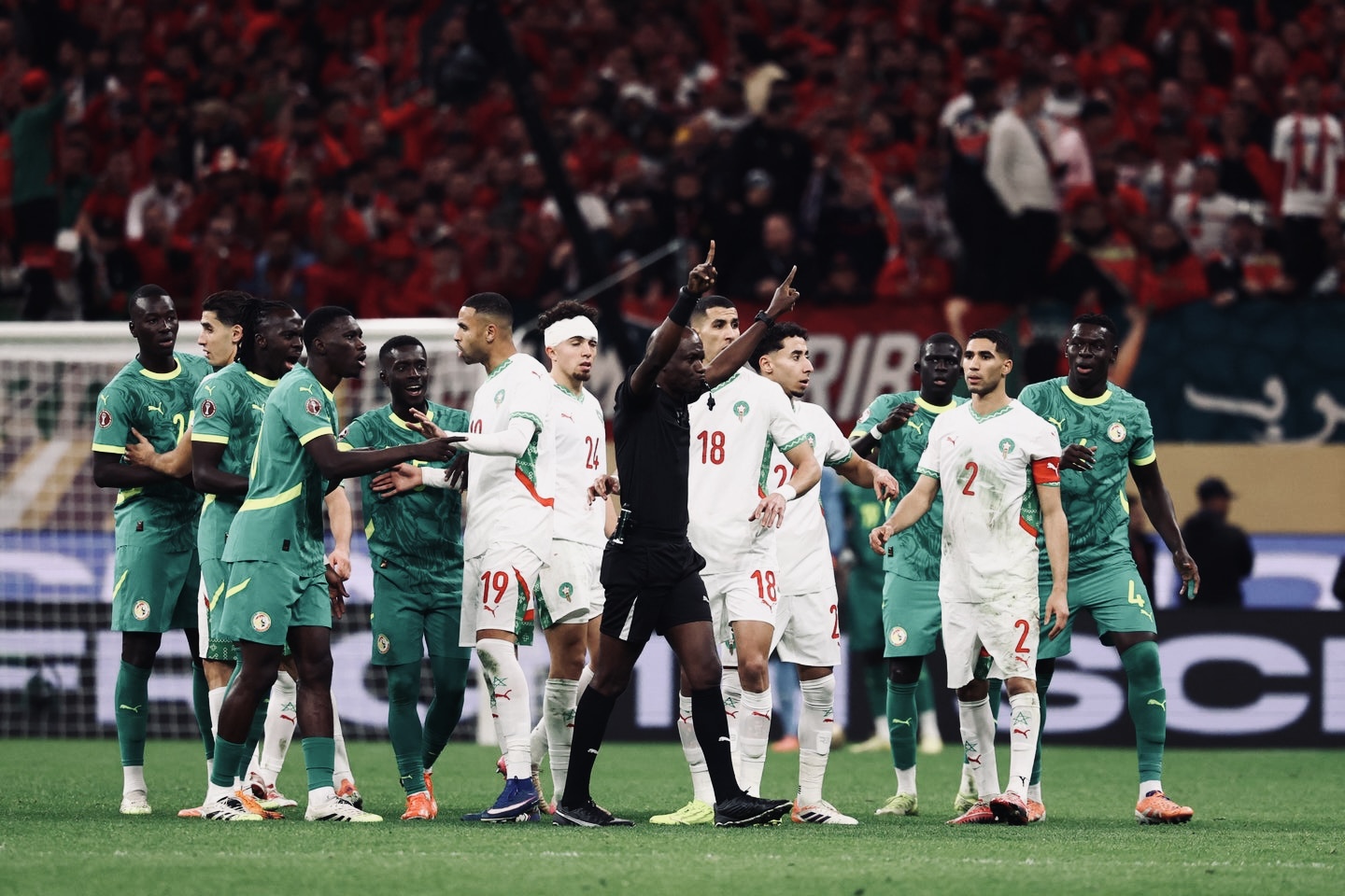 Jean-Jacques Ndala effectue le geste de la VAR au milieu des joueurs